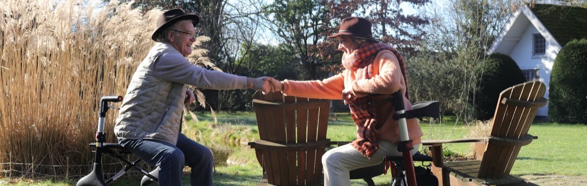 Two friends in hats shaking hands and laughing together in a sunny garden